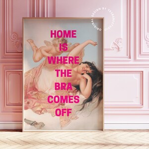 May include: A pink framed print with a painting of a woman reclining on a cloud with a cherub. The text "HOME IS WHERE THE BRA COMES OFF" is printed in pink on the print.