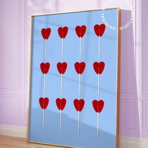 May include: A framed print of a blue background with twelve red heart-shaped lollipops on sticks. The lollipops are arranged in three rows of four. The print has a gold frame and the text "Original Design by Yes Babe Studio" is printed in a circle around the frame.
