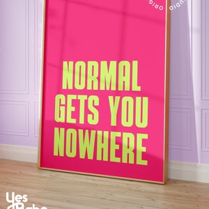 May include: A pink framed print with the text "NORMAL GETS YOU NOWHERE" in yellow lettering. The print is framed in a gold frame and has a white background.