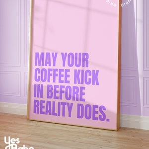Pode incluir: Um pôster emoldurado rosa com o texto "MAY YOUR COFFEE KICK IN BEFORE REALITY DOES." em letras roxas. O pôster está pendurado em uma parede de cor lilás claro.