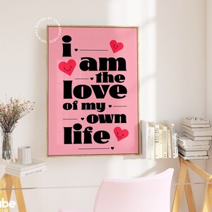 May include: Pink and black typography print with the text "I am the love of my own life" with red hearts with smiley faces.