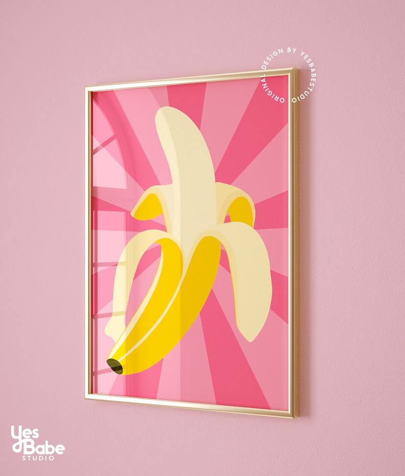 May include: A framed print of a yellow banana on a pink background with a sunburst pattern. The print is in a gold frame.
