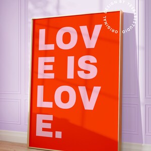 Może przedstawiać: Wydruk w ramie z czerwonym tłem i tekstem "LOVE IS LOVE." w r&oacute;żowych literach. Rama jest złota.