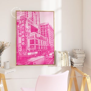 Op de afbeelding: Een ingelijste roze en witte prent van een Chicago stadsgezicht. Het kunstwerk heeft een halftone stippenpatroon en het woord "CHICAGO" in grote letters. De prent wordt weergegeven in een gouden lijst en hangt aan een witte muur.
