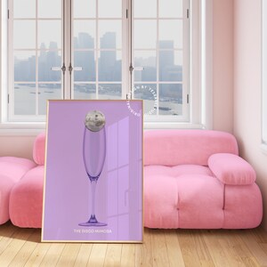May include: A purple poster with a gold frame featuring a glass of champagne with a disco ball inside. The text "The Disco Mimosa" is at the bottom of the poster.