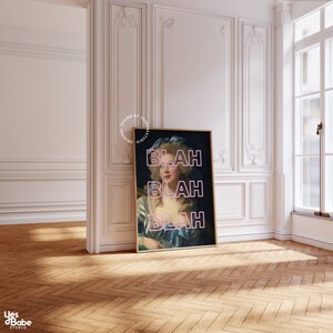 May include: A framed art print featuring a portrait of a woman in a blue dress and a blue bow. The word "BLAH" is stacked three times in pink neon letters over the portrait. The print is displayed in a room with white walls and a wooden floor.