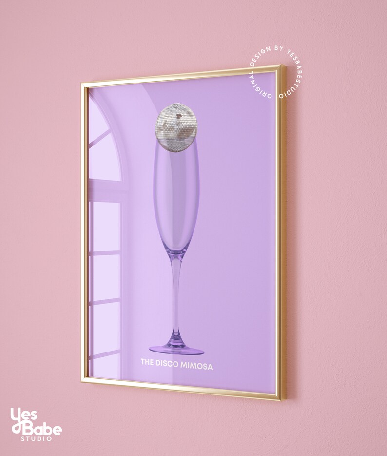 May include: A framed print with a purple background featuring a champagne flute with a disco ball on top. The text "THE DISCO MIMOSA" is printed below the glass. The frame is gold.