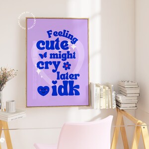 May include: A purple and blue poster with the text "Feeling cute might cry later idk" in a heart shape. The poster is framed in a gold frame and hanging on a white wall.