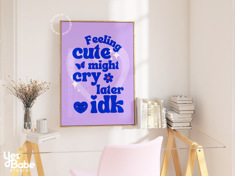 May include: A purple and blue poster with the text "Feeling cute might cry later idk" in a heart shape. The poster is framed in a gold frame and hanging on a white wall.