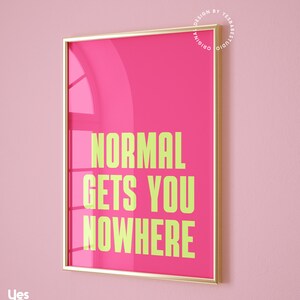 May include: A framed pink poster with gold trim. The poster has the text "NORMAL GETS YOU NOWHERE" in yellow.