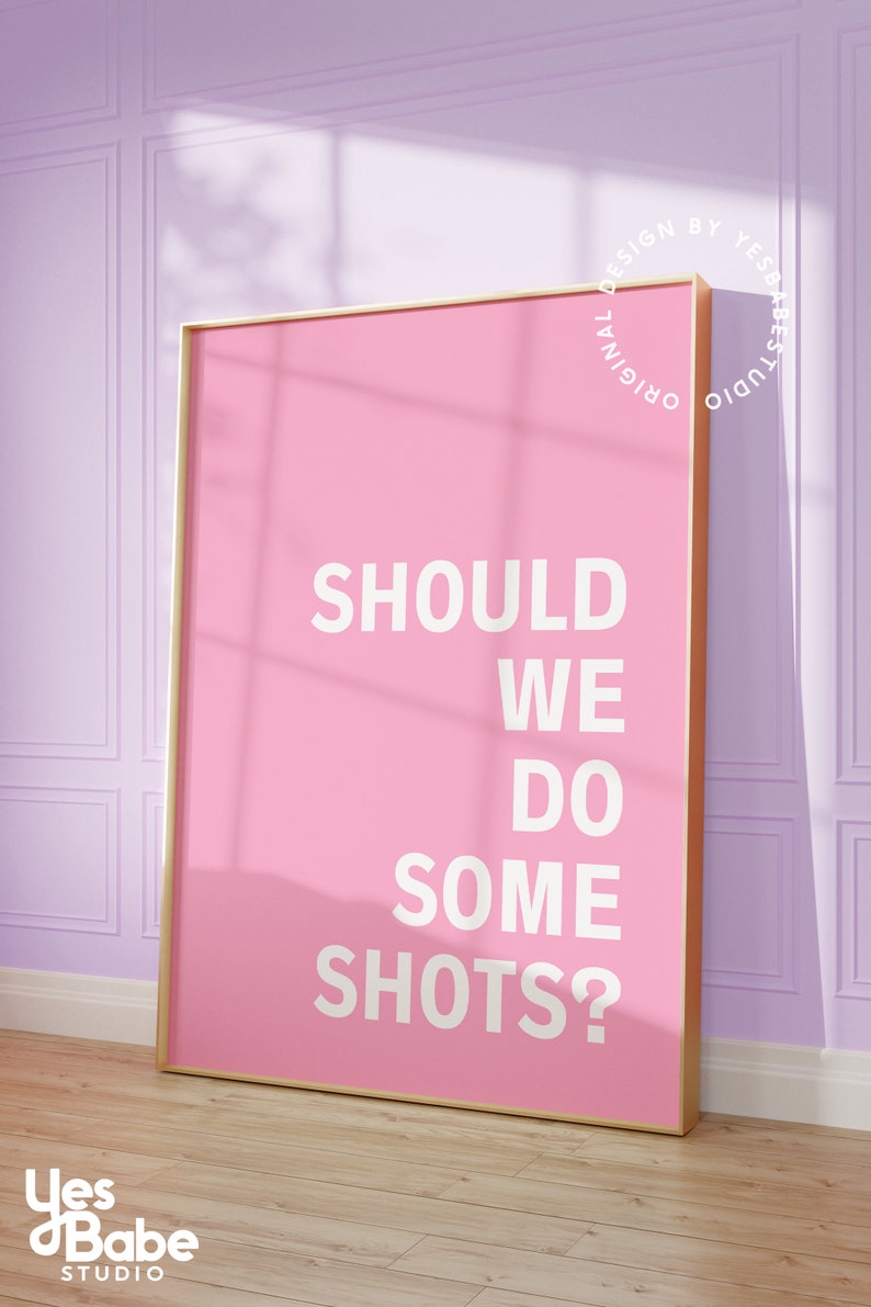 May include: A pink framed poster with the text "Should we do some shots?" in white lettering. The poster is hanging on a light purple wall.