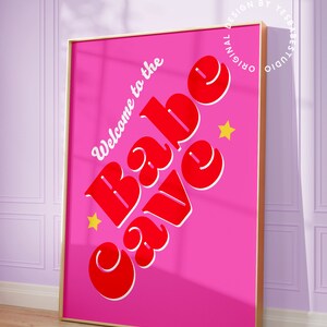Puede incluir: Una impresi&oacute;n enmarcada rosa con el texto "Welcome to the Babe Cave" en letras rojas y blancas con dos estrellas amarillas.