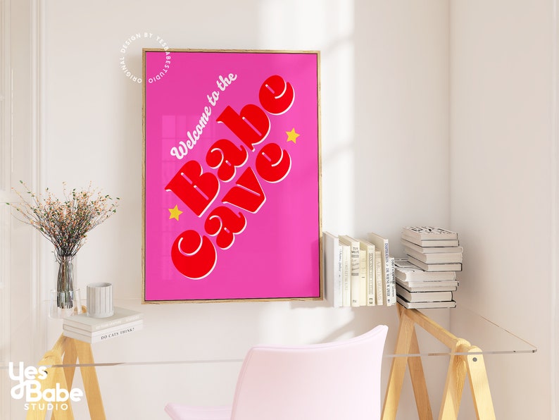 Puede incluir: Un p&oacute;ster rosa y rojo con el texto "Welcome to the Babe Cave" en una fuente retro. El p&oacute;ster est&aacute; enmarcado en oro y tiene dos estrellas amarillas.