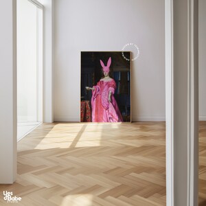 May include: A painting of a woman in a pink dress and a pink bunny mask, standing in a room with a red rug and a dark background. The painting is framed in a wooden frame.