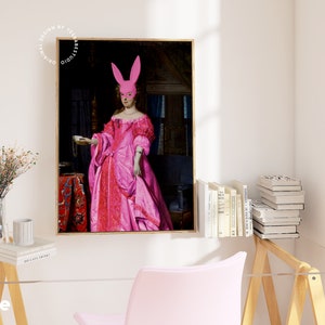 May include: A painting of a woman in a pink dress wearing a pink bunny mask. The woman is holding a small cup in her hand. The painting is set in a dark room with a red rug on the floor.