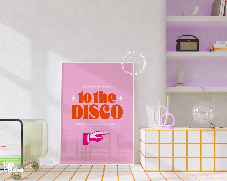 May include: Pink poster with a white border featuring a red and orange graphic that says "to the disco" with a pointing hand. The poster is hanging on a white wall.