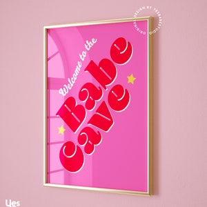 Puede incluir: Una impresi&oacute;n enmarcada rosa con el texto "Welcome to the Babe Cave" en letras rojas con un contorno blanco. Dos estrellas amarillas est&aacute;n a cada lado del texto.