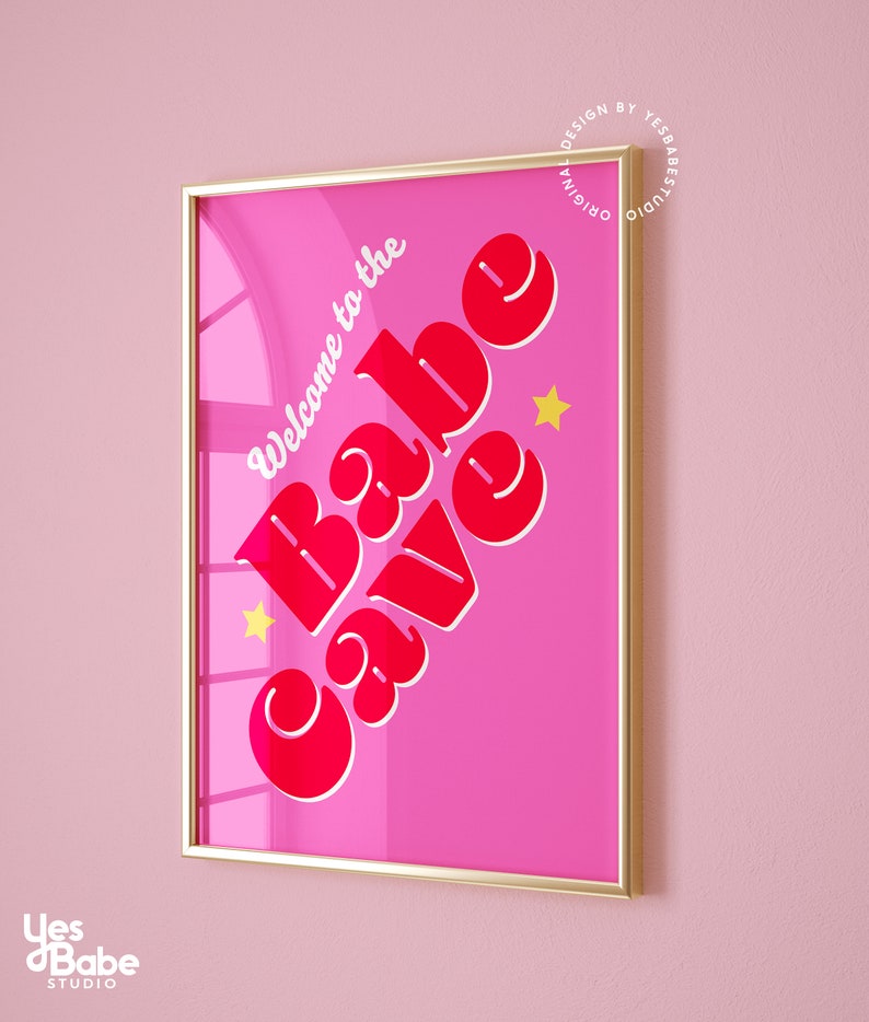 Puede incluir: Una impresi&oacute;n enmarcada rosa con el texto "Welcome to the Babe Cave" en letras rojas con un contorno blanco. Dos estrellas amarillas est&aacute;n a cada lado del texto.