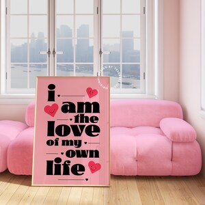 May include: A pink framed poster with black text that reads "i am the love of my own life" with red hearts with smiley faces on them.