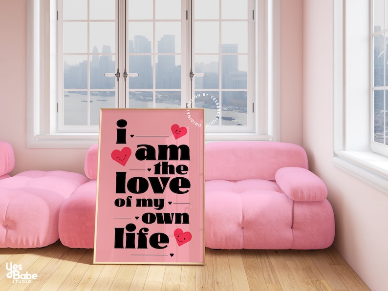 May include: A pink framed poster with black text that reads "i am the love of my own life" with red hearts with smiley faces on them.