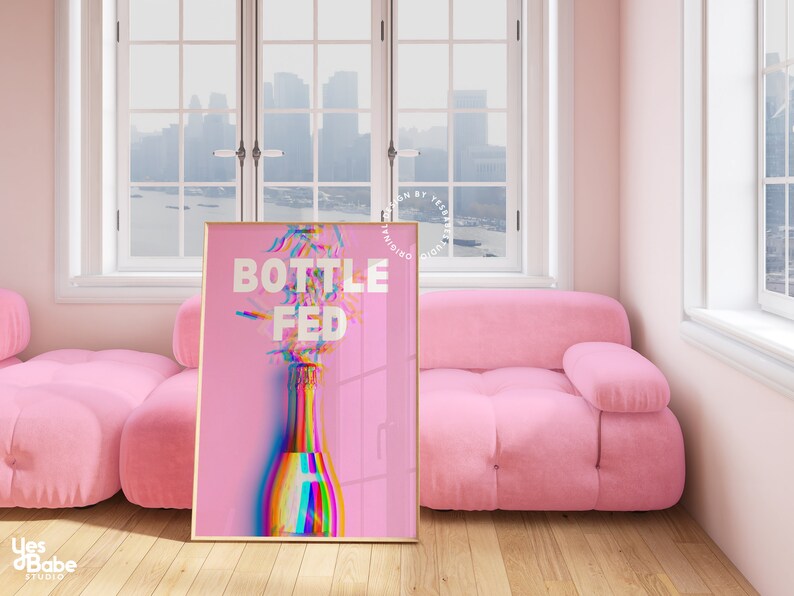 May include: A pink poster with a gold frame featuring a rainbow-colored champagne bottle with the text "Bottle Fed" in white.