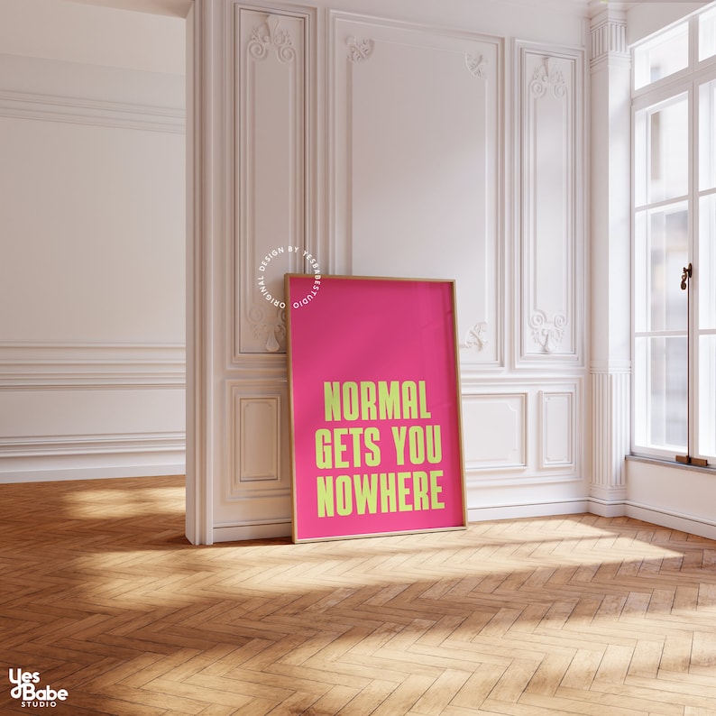 May include: A pink poster with the text "NORMAL GETS YOU NOWHERE" in yellow letters. The poster is framed in a thin, wooden frame and is hanging on a white wall.