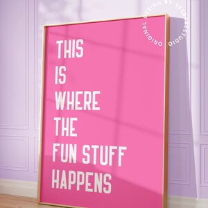 Puede incluir: P&oacute;ster rosa con marco dorado y texto blanco que dice "This is where the fun stuff happens". El p&oacute;ster est&aacute; colgado en una pared morada.