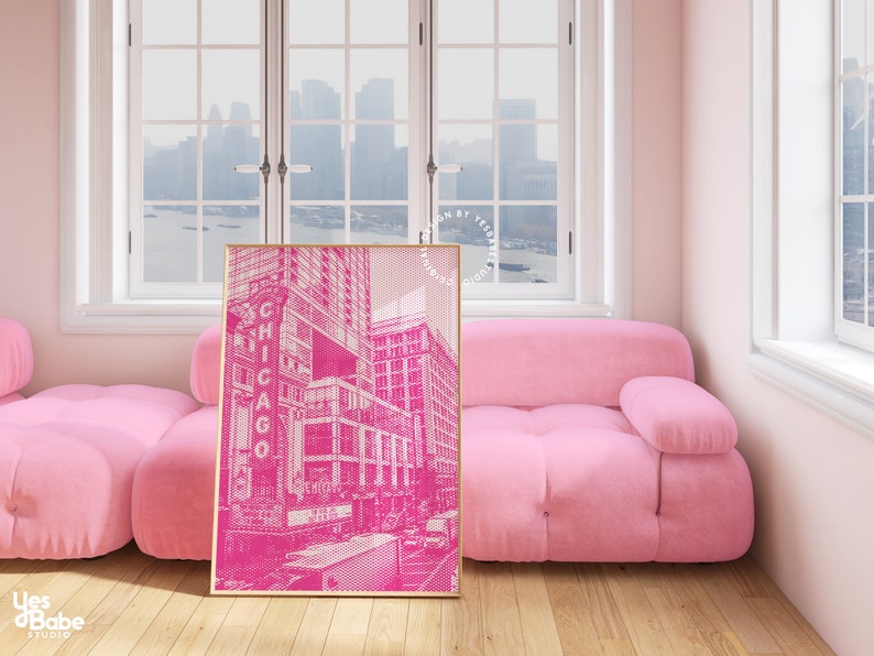 Op de afbeelding: Een ingelijste roze en witte prent van een Chicago straatbeeld, leunend tegen een roze bank. De prent toont het woord "CHICAGO". De kamer heeft een roze kleurenschema met een raam op de achtergrond.