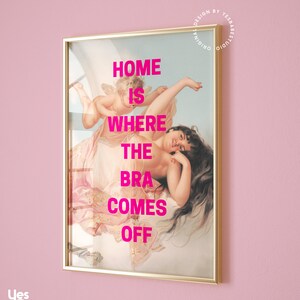 May include: A framed print with a gold frame and a painting of a woman with a cherub. The text "HOME IS WHERE THE BRA COMES OFF" is printed in pink on the painting.