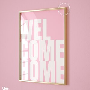 May include: A gold framed print with a pink background and white text that reads "WELCOME HOME".
