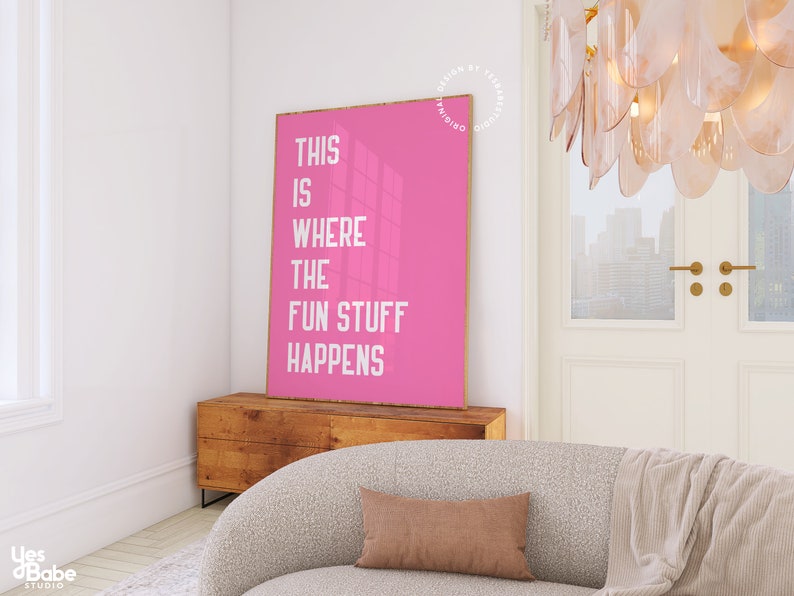 Puede incluir: P&oacute;ster rosa con texto blanco que dice "This is where the fun stuff happens". El p&oacute;ster est&aacute; colgado en una pared blanca en una habitaci&oacute;n con un sof&aacute; y una c&oacute;moda de madera.