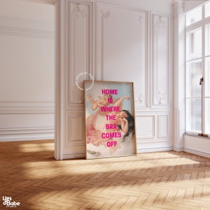 May include: A framed print with a painting of a woman and a cherub. The text "HOME IS WHERE THE BRA COMES OFF" is printed in pink on the print.