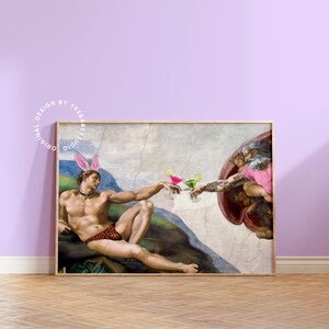 May include: A humorous parody of the famous "The Creation of Adam" painting, featuring two men in a similar pose, but holding cocktails instead of touching fingers. The man on the left is wearing a pink bunny ear headband and a leopard print swimsuit. The man on the right has a tattoo that says "Big Daddy" and is wearing a pink shirt. The painting is framed in a wooden frame.