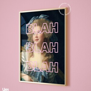 May include: Framed art print featuring a portrait of a woman with a blue bow and dress, overlaid with the word "BLAH" in pink three times. The artwork is in a gold frame, set against a pink wall. The print is from Yes Babe Studio.