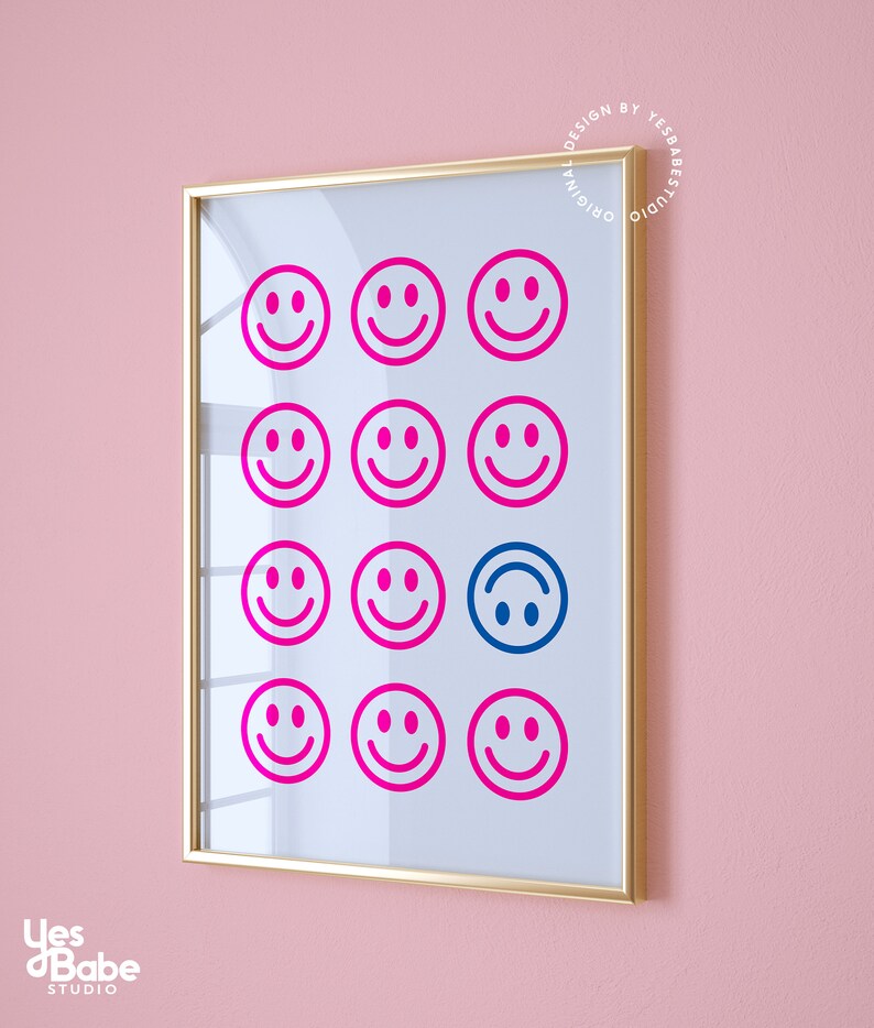 Pu&ograve; includere: Una stampa incorniciata con sfondo bianco e una griglia di 12 facce sorridenti rosa. La faccia sorridente al centro in basso &egrave; blu e capovolta. La cornice &egrave; dorata.