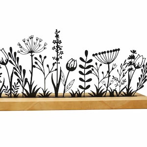 Könnte beinhalten: Dekorative Blumensilhouette aus schwarzem Metall. Das Design zeigt verschiedene stilisierte Blumen und Blätter auf einem Naturholzsockel. Ein dekoratives Element für Haus oder Garten.