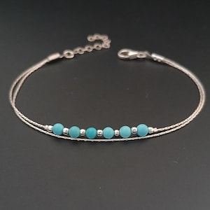 Könnte beinhalten: Ein zartes Armband aus Silberkette mit einer Reihe von türkisfarbenen Perlen. Das Armband hat einen Karabinerverschluss.