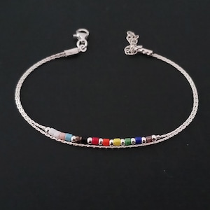 Peut inclure: Un bracelet en argent avec une fine chaîne. Il présente une rangée de petites perles multicolores disposées en arc-en-ciel. Le fermoir est de type homard.