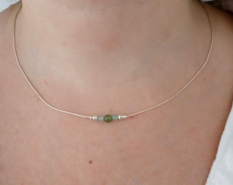 May include: Delicate silver necklace featuring a small, round, green gemstone bead flanked by two smaller, pale green beads and silver accents. The necklace is strung on a fine silver chain, creating a minimalist and elegant design.