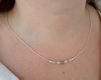 May include: A delicate silver necklace featuring a string of small, colorful beads. The beads are a mix of pale pink, light green, and silver, strung on a thin silver chain. The necklace is designed to be worn around the neck.