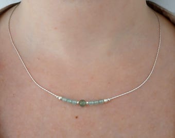 May include: A delicate silver necklace featuring a strand of small, light green beads interspersed with silver accents. The necklace is worn around the neck, showcasing its minimalist design and subtle color palette. The beads are approximately 0.2 inches in diameter.