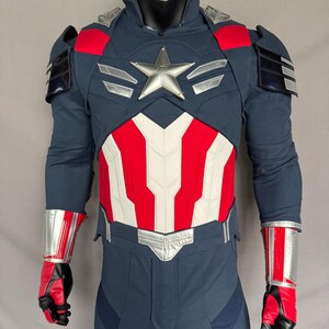 Puede incluir: Un traje de superh&eacute;roe azul y rojo con una estrella plateada en el pecho. El traje tiene un cintur&oacute;n plateado y detalles plateados en los brazos y las piernas.