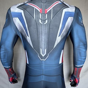May include: A blue, gray, white, and red bodysuit costume. The back of the suit features a detailed design with geometric shapes and lines. The sleeves and lower legs are blue, with red and black accents on the wrists and ankles. The suit is form-fitting.