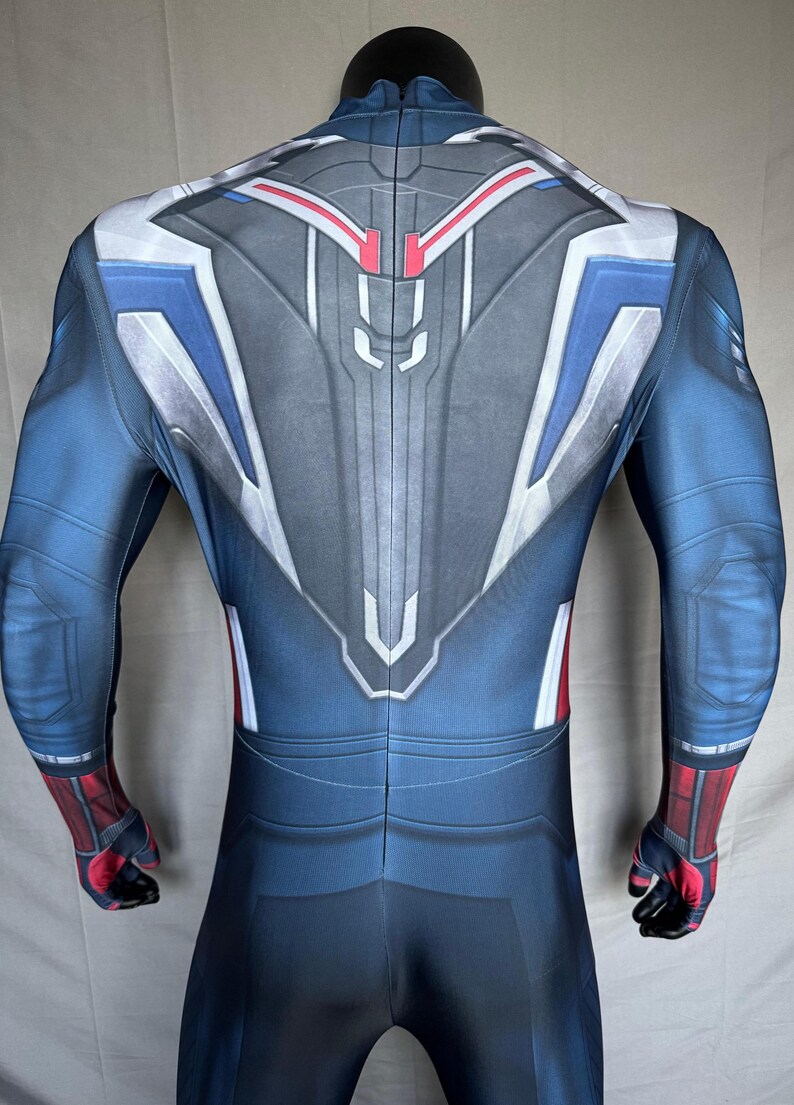 May include: A blue, gray, white, and red bodysuit costume. The back of the suit features a detailed design with geometric shapes and lines. The sleeves and lower legs are blue, with red and black accents on the wrists and ankles. The suit is form-fitting.
