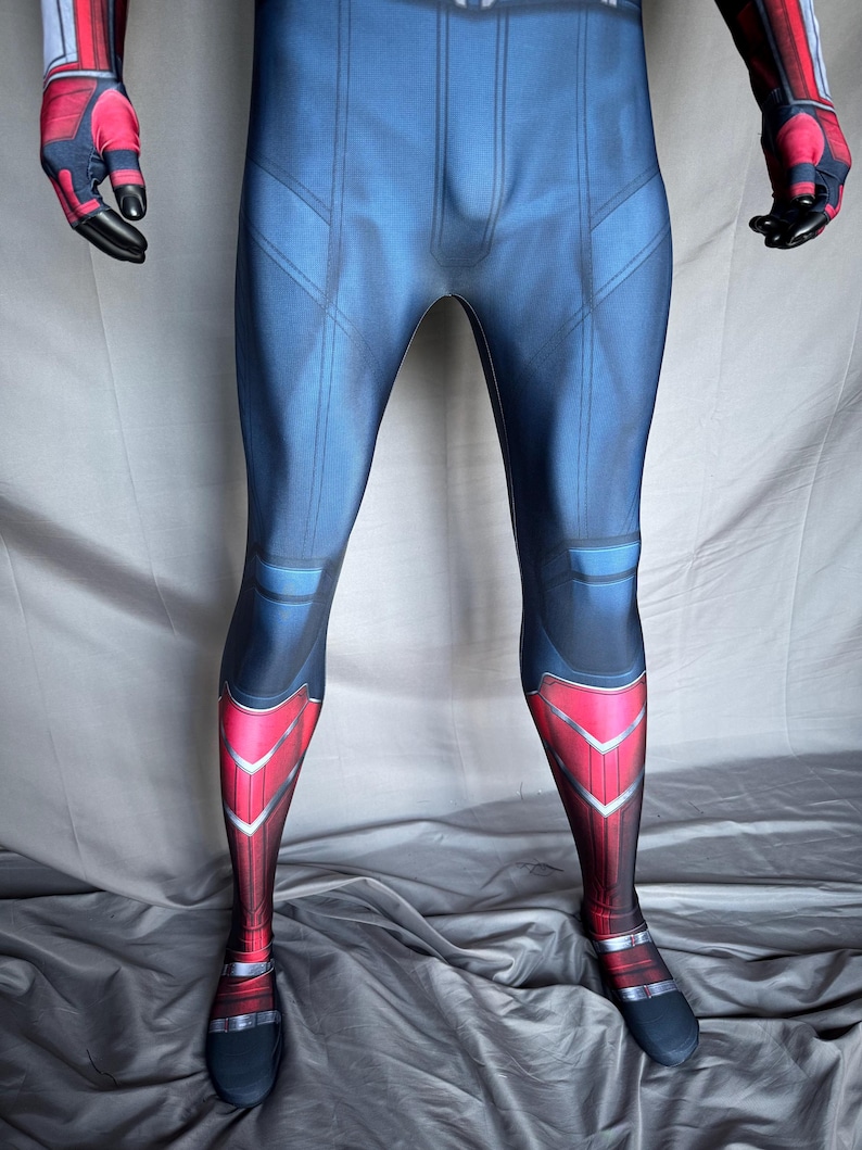 May include: A full-body superhero costume in blue, red, and black. The costume features a blue torso with red accents on the legs and arms. The gloves and feet are black. The design includes geometric patterns and lines.