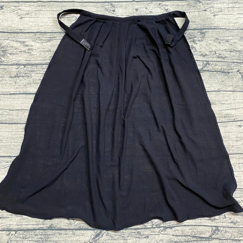 May include: A black wrap skirt with a simple design and adjustable straps. The skirt is made of a soft, lightweight fabric.
