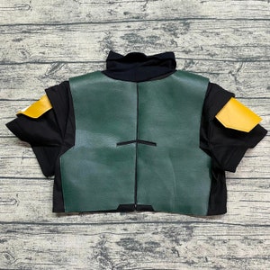 May include: A green and black costume vest with yellow shoulder pads. The vest has a black trim and a zipper in the back.