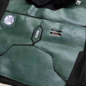 May include: A green leather jacket with black stitching and a patch with a symbol on the left chest. The jacket has a zipper and a label that says "DUEEP".
