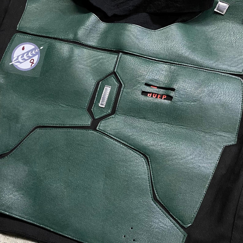 May include: A green leather jacket with black stitching and a patch with a symbol on the left chest. The jacket has a zipper and a label that says "DUEEP".