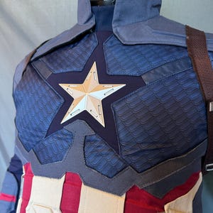 Puede incluir: Un traje de superh&eacute;roe azul y rojo con un emblema en forma de estrella en el pecho. El traje tiene una tela texturizada y un dise&ntilde;o acolchado.
